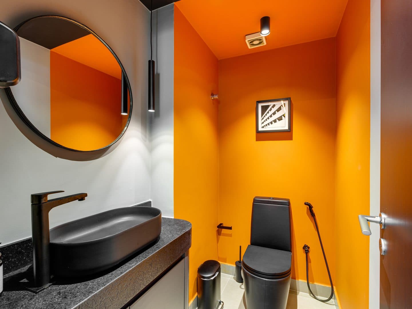 Lavabo com parede laranja, cuba preta e espelho redondo