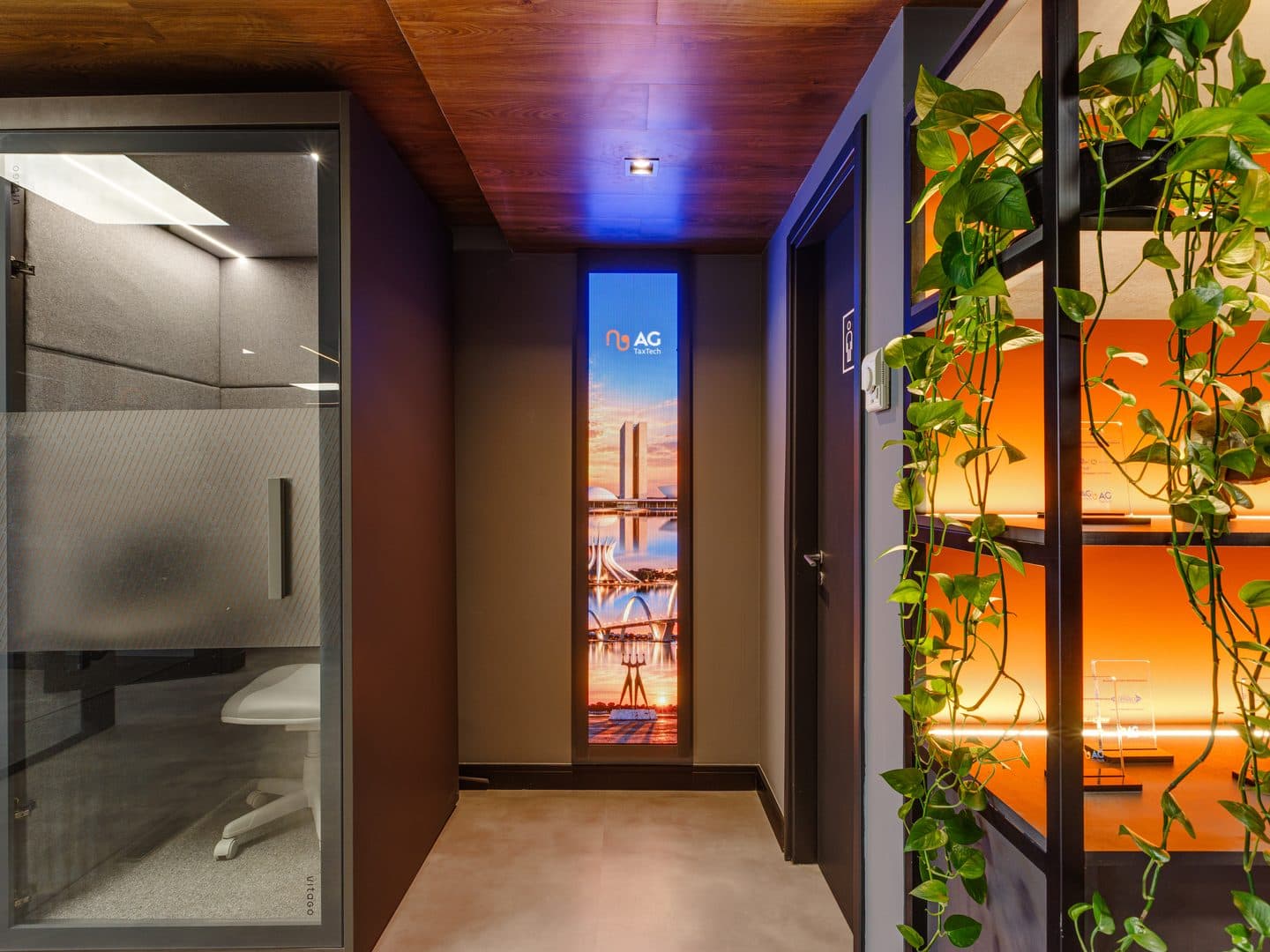 Corredor com estante iluminada, plantas e totem de marca